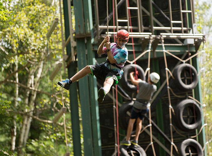 A camper smiles while holding onto the zipline rope and swings through the air at North Star Camp for Boys.