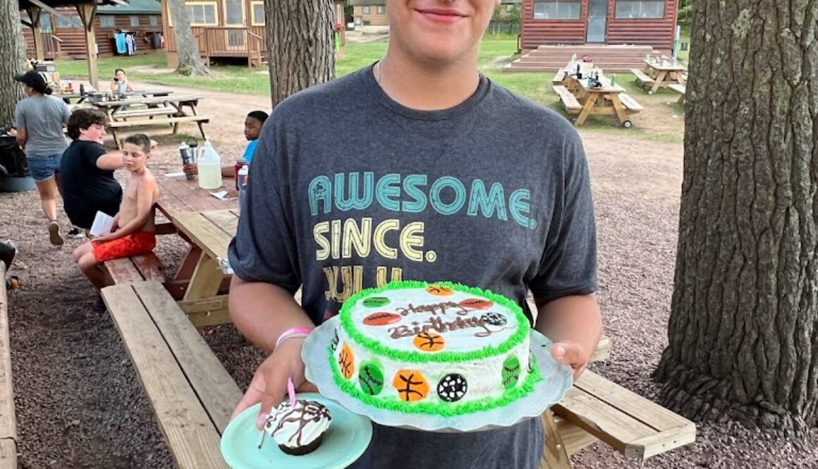 A camper at North Star Camp for Boys holds a birthday cake while smiling for a picture.