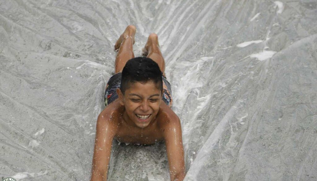A camper at North Star Camp for Boys smiles while sliding down a slip n' slide.
