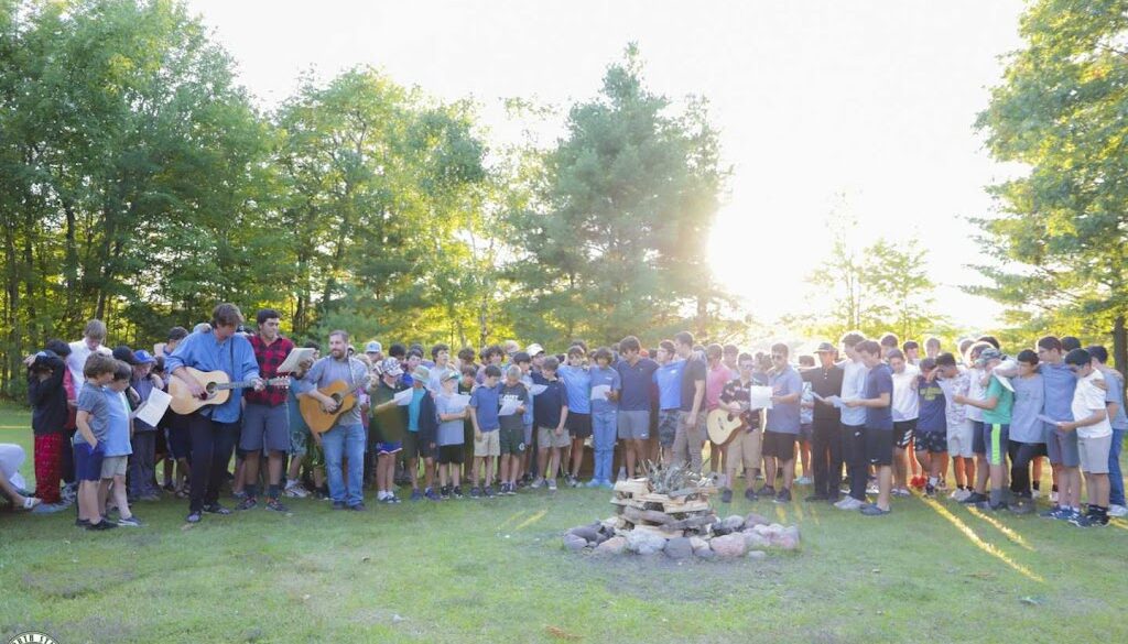 A group of campers and staff members gather around the fire pit to sing and play guitar at North Star Camp for Boys.