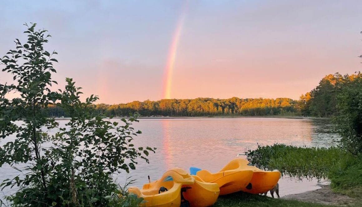 Fun bugs sit on the lakeshore at sunset, with a rainbow in the distance at North Star Camp for Boys.