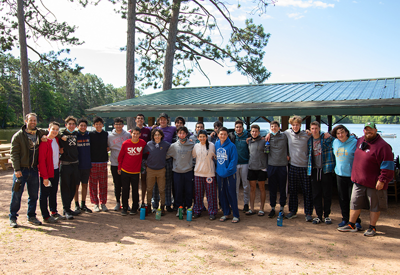 The staff members at North Star Camp for Boys gather around the lakeside and smile for a picture.