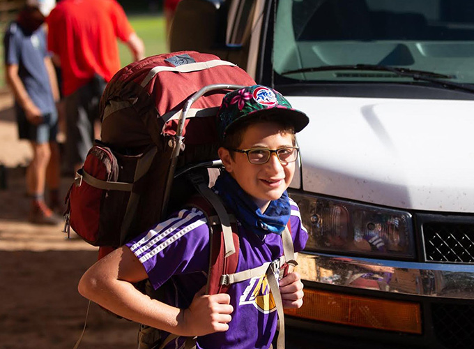 A camper wearing a hiking backpack smiles for a photo during a wilderness hiking trip at North Star Camp for Boys.