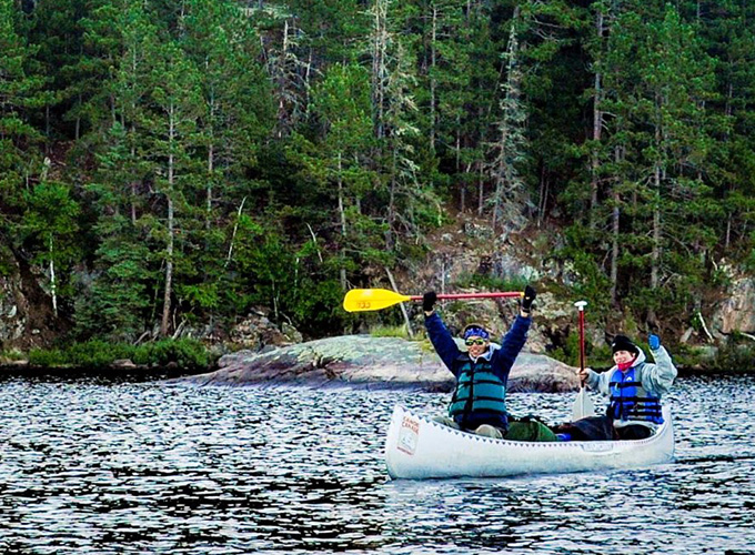 Two boys at North Star Camp are in a canoe holding up their ores in a cheering motion.