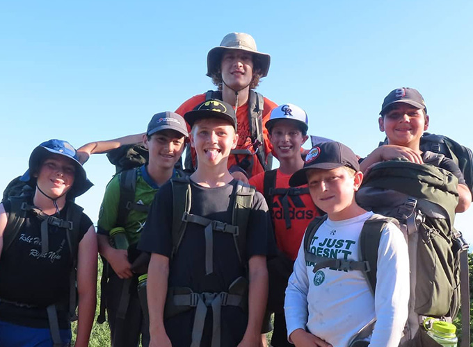 A staff member smiles for a photo with a group of campers during a hiking wilderness trip at North Star Camp for Boys.