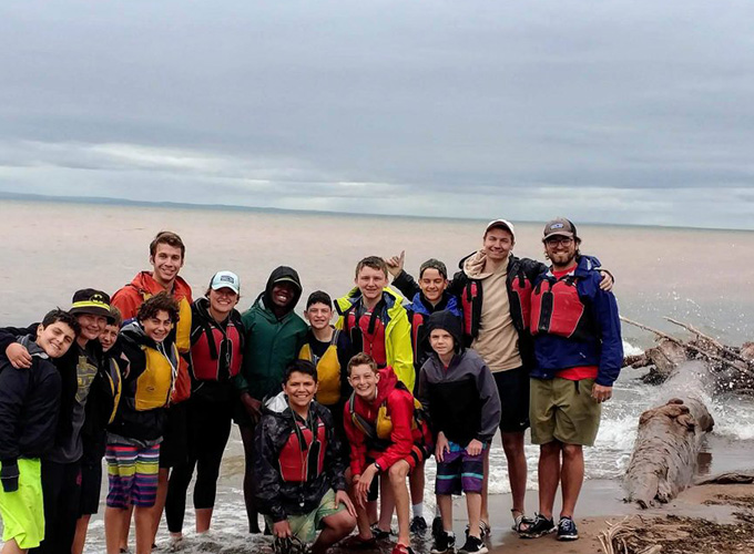 A group of campers and staff members at North Star Camp for Boys smile for a photo on the shoreline during a Wilderness Trip.
