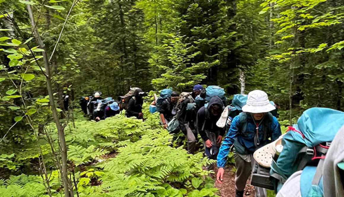 A group of campers and staff members walk single-file through a hiking trail during a wilderness trip at North Star Camp for Boys.