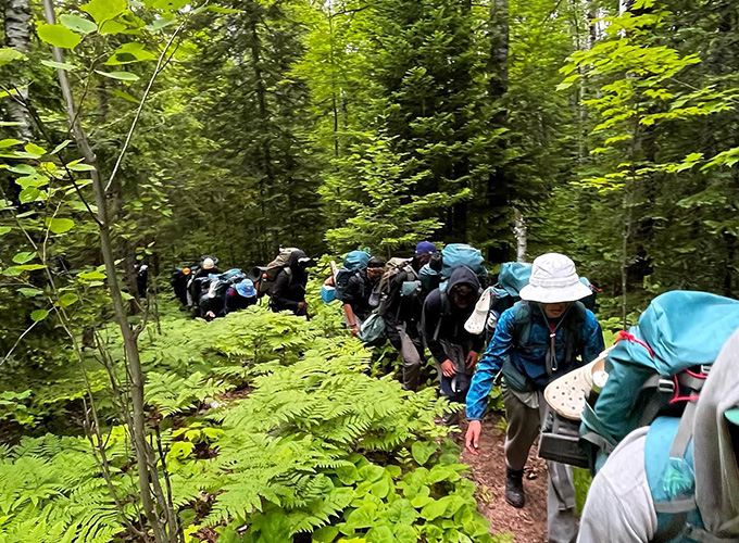 A group of campers and staff members walk single-file through a hiking trail during a wilderness trip at North Star Camp for Boys.