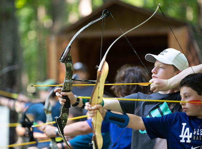 Campers pull back the strings on an archery bow and aim their arrows during archery training at North Star Camp for Boys.