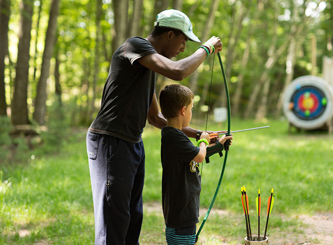 A counselor helps a camper attach and aim a bow to an arrow during an archery activity at North Star Camp for Boys.