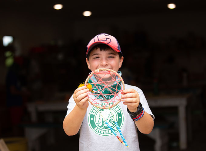 A camper holds up a homemade dream catcher and smiles for a photo at North Star Camp for Boys.