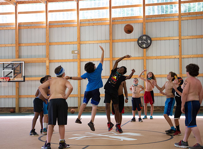 A group of campers watch as two boys jump for a basketball at the indoor gym of North Star Camp for Boys.