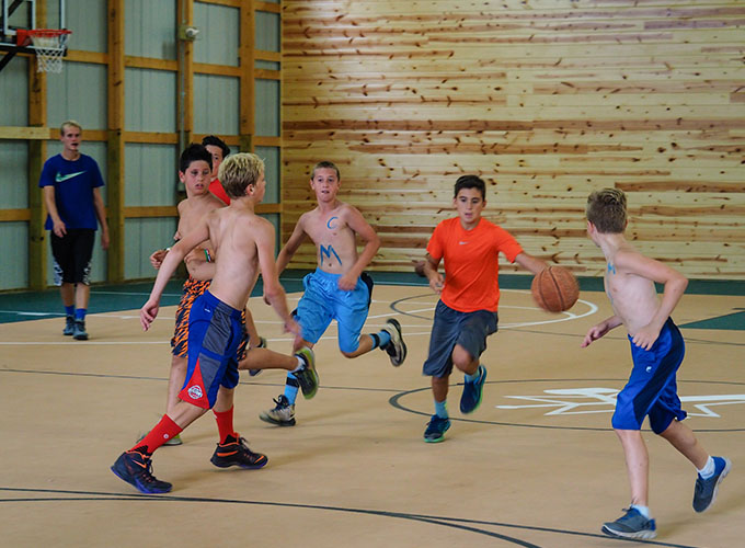 A group of campers run in the indoor gym while one camper dribbles a basketball at North Star Camp for Boys.