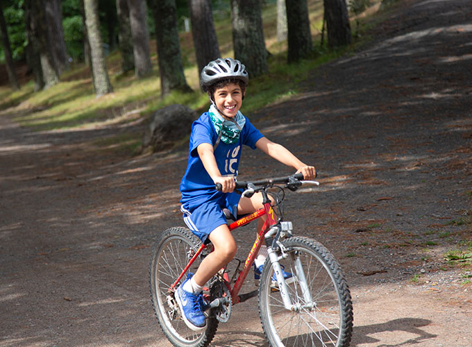 A camper smiles while riding his bike through the woodsy trails of North Star Camp for Boys.