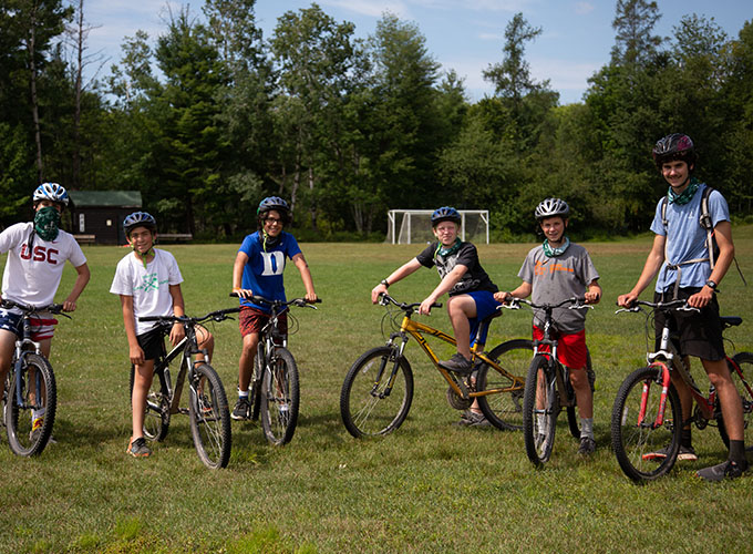 A group of six campers smile for a photo while on bikes and wearing bike helmets at North Star Camp for Boys.