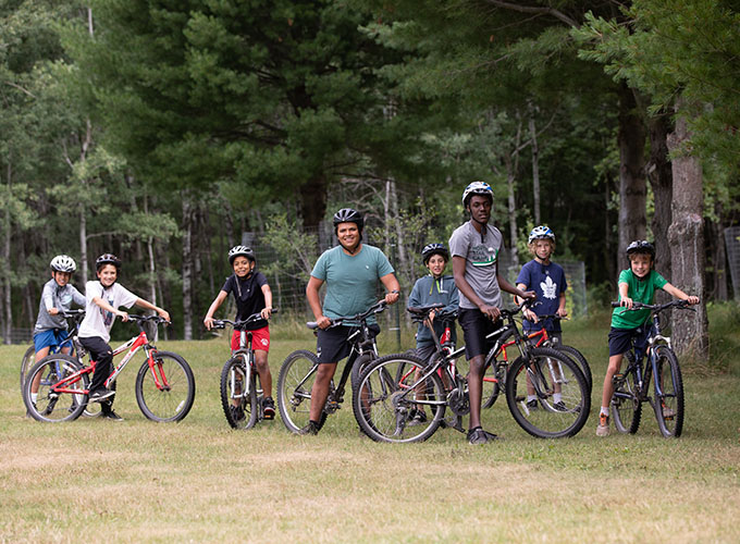 A group of campers and two staff members smile for a photo while enjoying a bike ride through the campgrounds of North Star Camp for Boys.