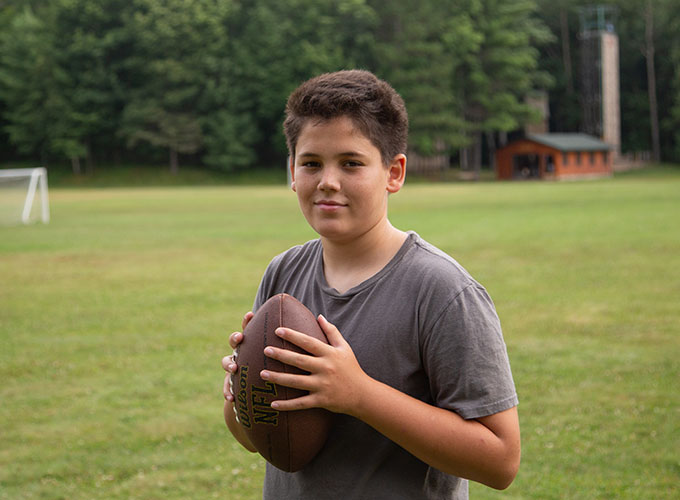 A camper holds a football while standing in a field at North Star Camp for Boys.