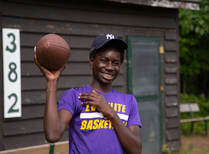 A camper smiles while holding up a football with one hand at North Star Camp for Boys.