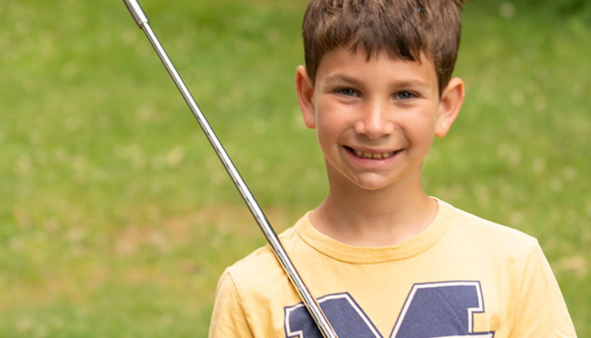 A camper at North Star Camp for Boys smiles while holding up a golf club.