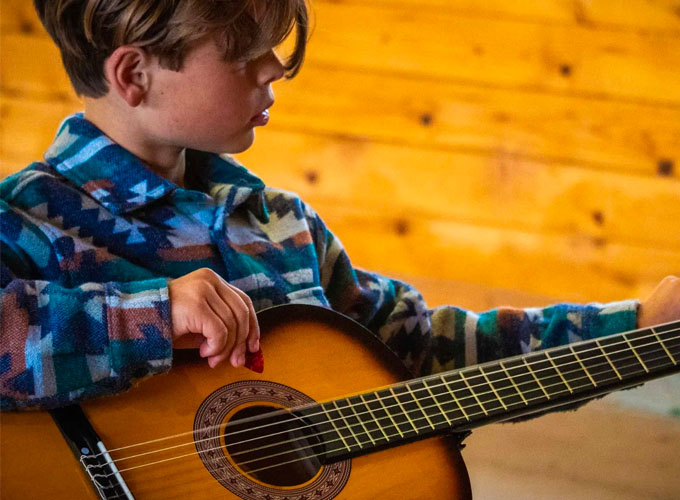 A camper at North Star Camp for Boys holds a guitar during an activity session.