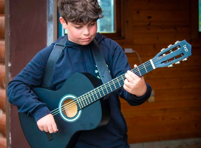 A camper at North Star Camp for Boys strums a guitar during an activity session.