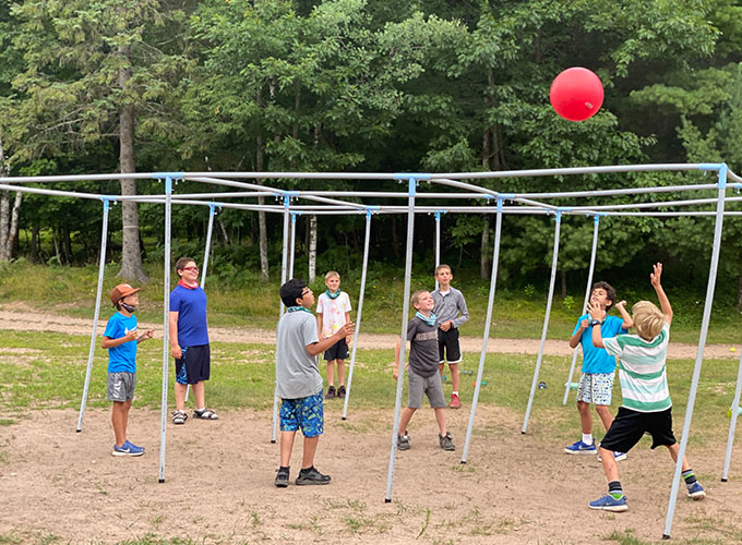 A group of elementary-aged boys at North Star Camp for Boys play a game of nine square in the air, in which they stand in a designated spot and hit a large, red ball to other players.