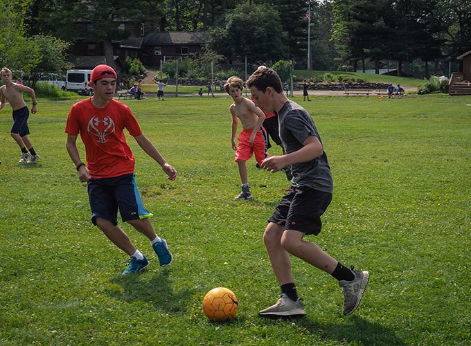 A group of boys at North Star Camp for Boys kick around a soccer ball, as tries to take over the ball from his teammate.