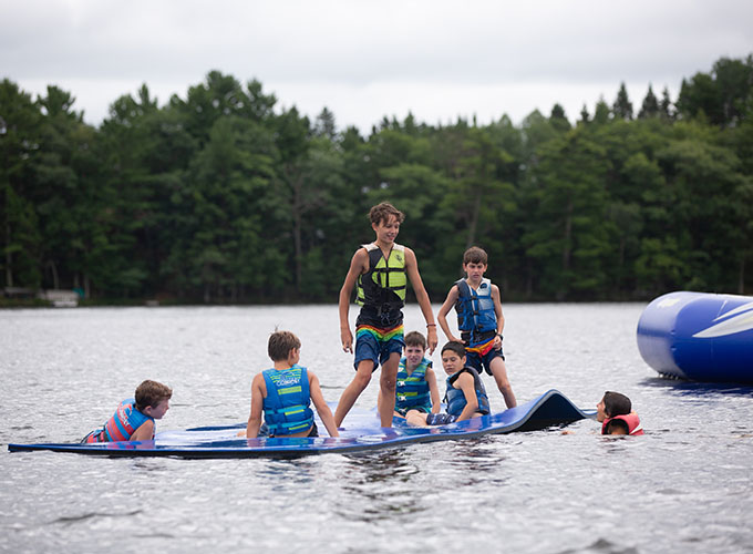 A group of boys sit and stand on the splash mat in Spider Lake, at North Star Camp for Boys.