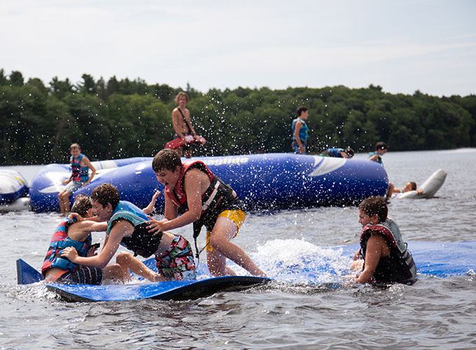 A group of boys splash on the "blob", a mat that allows people to stand on water in Spider Lake, at North Star Camp for Boys.