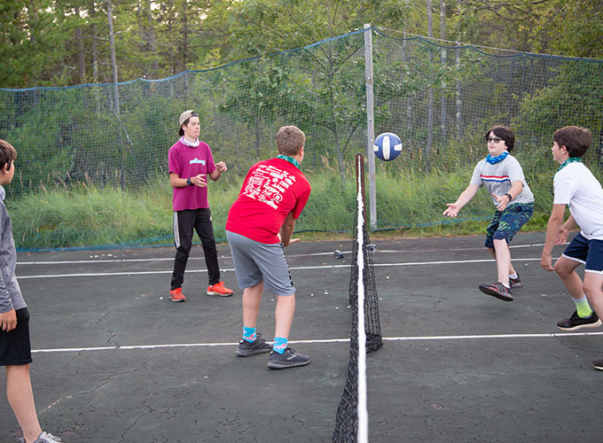 A group of campers at North Star Camp for Boys stand on a tennis court and toss around a volleyball.
