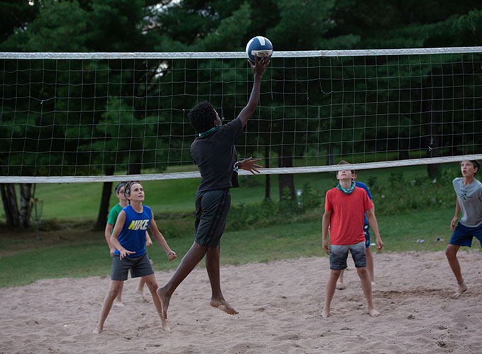 A camper jumps up to bump a volleyball over the net while his opponents prepare their next move at North Star Camp for Boys.