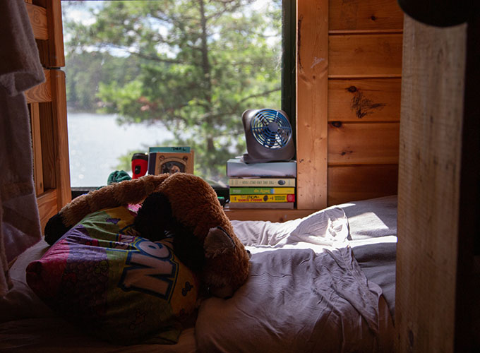 A bed with a window looking out to Spider Lake at North Star Camp for Boys.