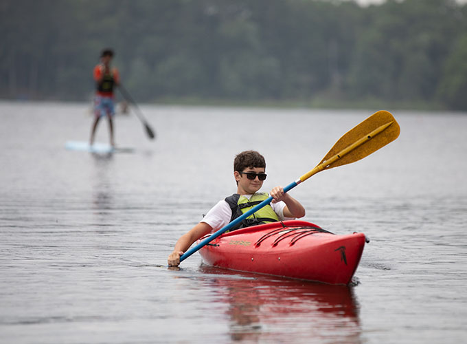 A camper at North Star Camp for Boys paddles through Spider Lake while sitting in a kayak.