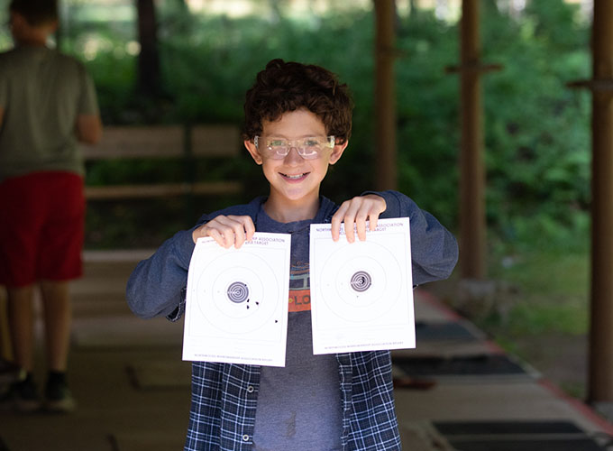 A camper at North Star Camp for Boys wearing protective safety glasses holds up the bullseye target he was aiming at during a riflery activity session.