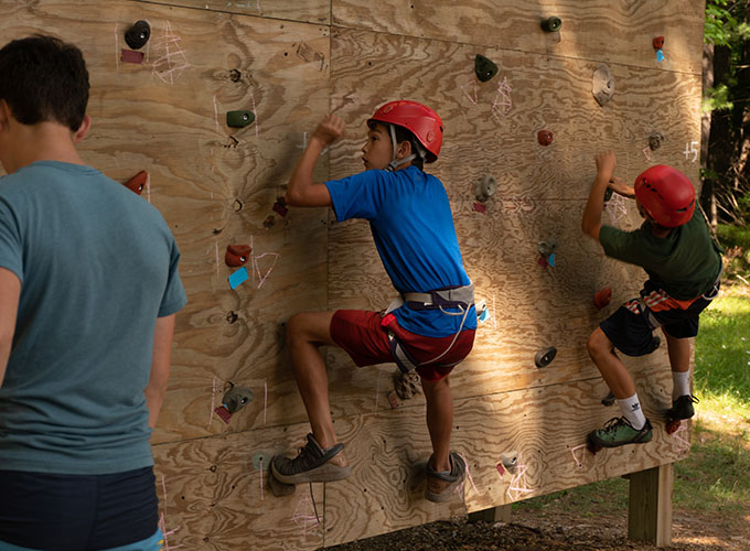 Campers wear hard hats as they begin climbing up the rock wall at North Star Camp for Boys.