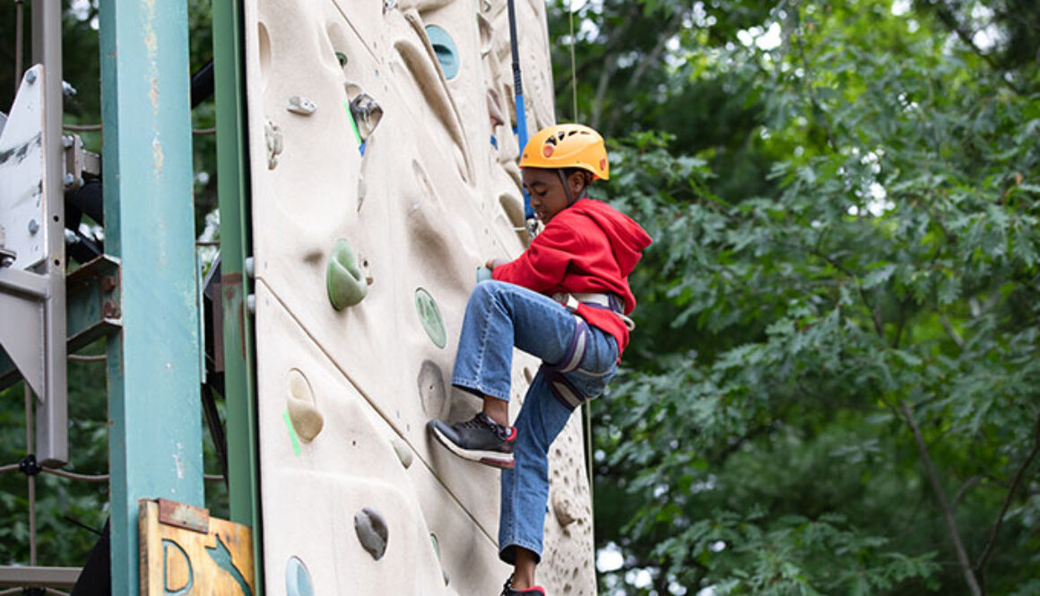 A camper looks down as he positions his feet while climbing up the rock wall at North Star Camp for Boys.