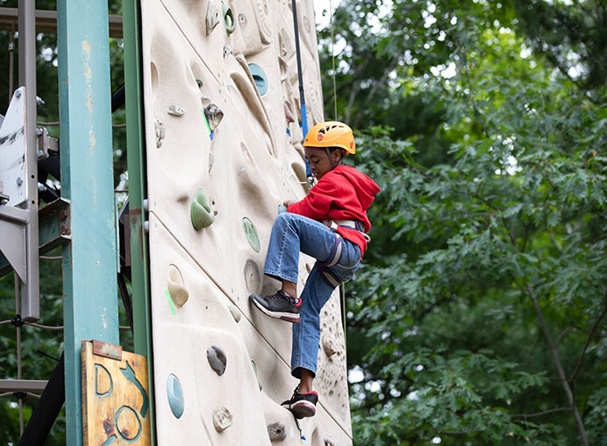 A camper looks down as he positions his feet while climbing up the rock wall at North Star Camp for Boys.