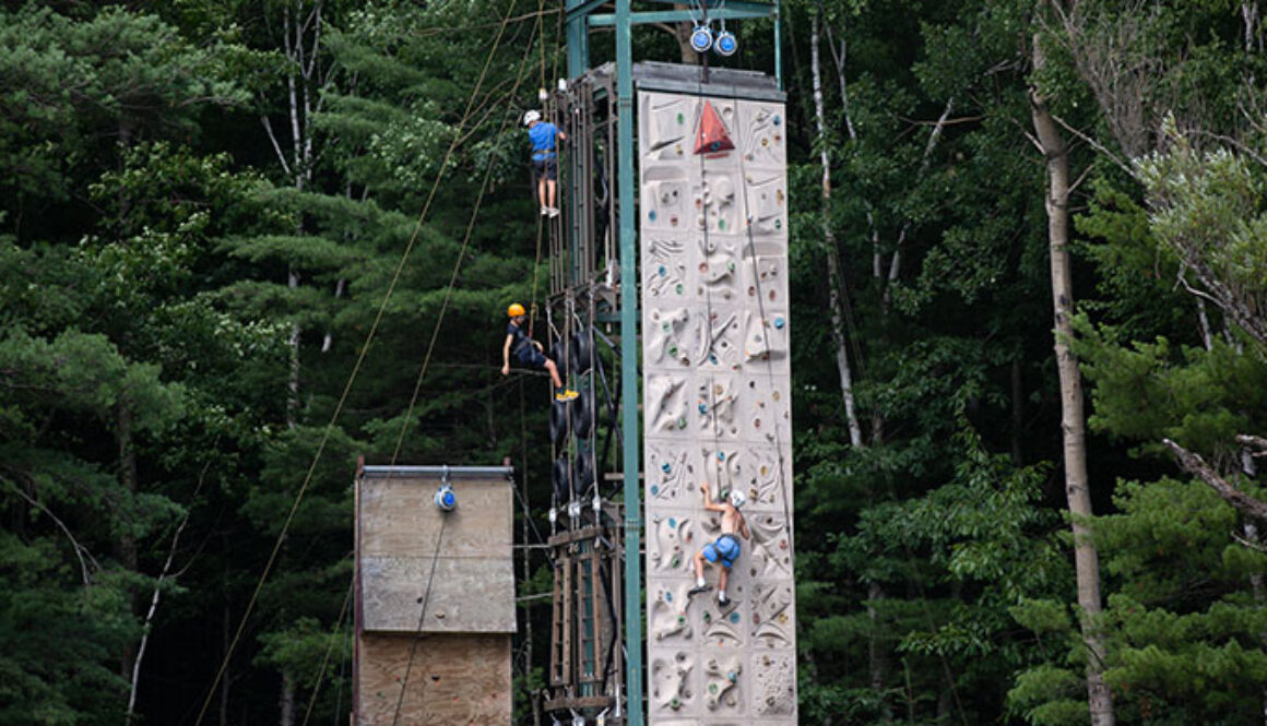 Campers climb up the sides of a climbing wall tower at North Star Camp for Boys.