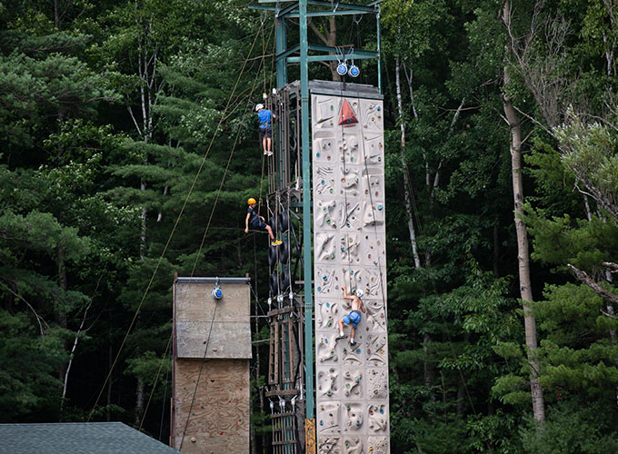 Campers climb up the sides of a climbing wall tower at North Star Camp for Boys.
