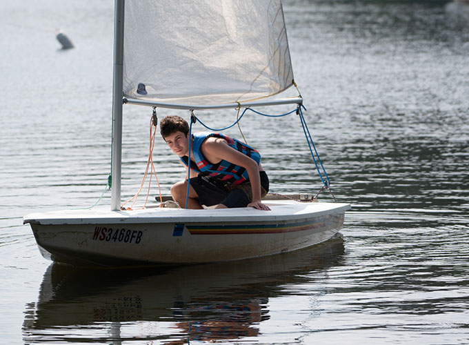 A camper wears a life jacket while ducking under the sails of a sailboat on Spider Lake at North Star Camp for Boys.