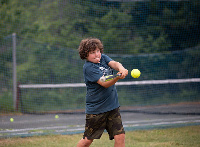 A camper at North Star Camp for Boys focuses on the incoming softball, as he swings the bat to it.