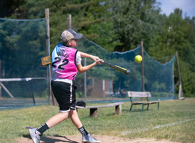 A camper at North Star Camp for Boys stands on first base swinging a bat at an incoming softball.