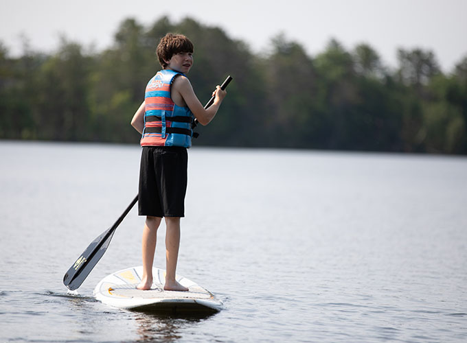 A camper enjoys the surroundings of Spider Lake, as he stand-up paddleboards at North Star Camp for Boys.