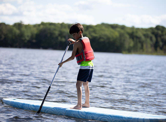 A camper dips an ore into Spider Lake while stand-up paddle boarding at North Star Camp for Boys.