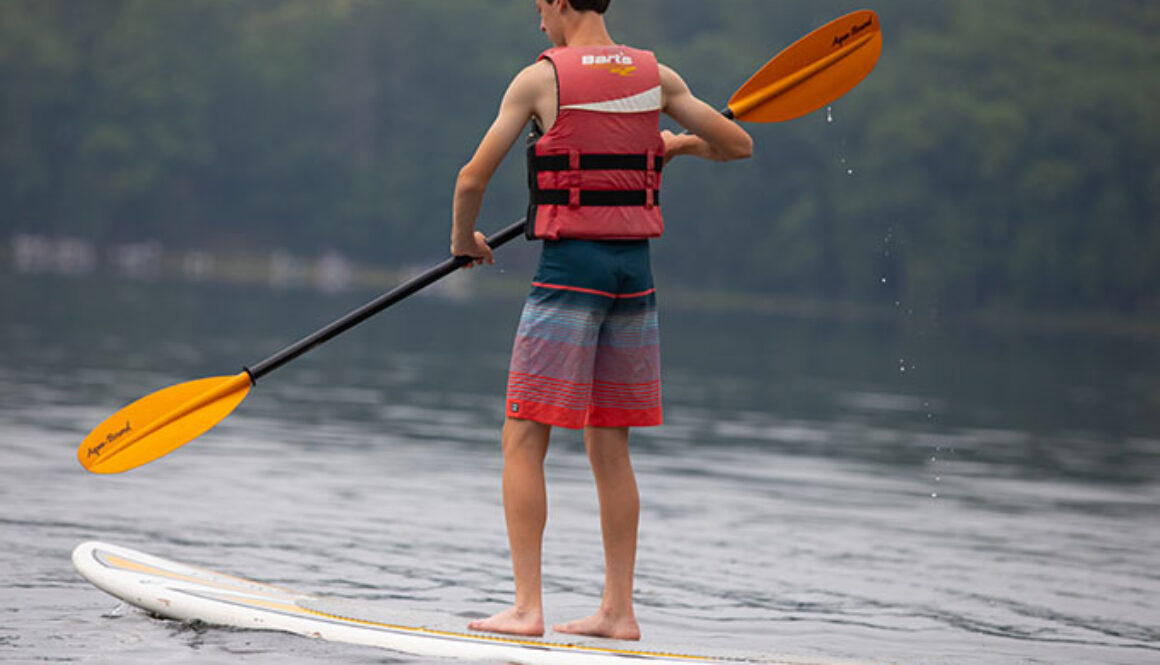 A camper wears a life jacket and stand-up paddleboards on Spider Lake at North Star Camp for Boys.