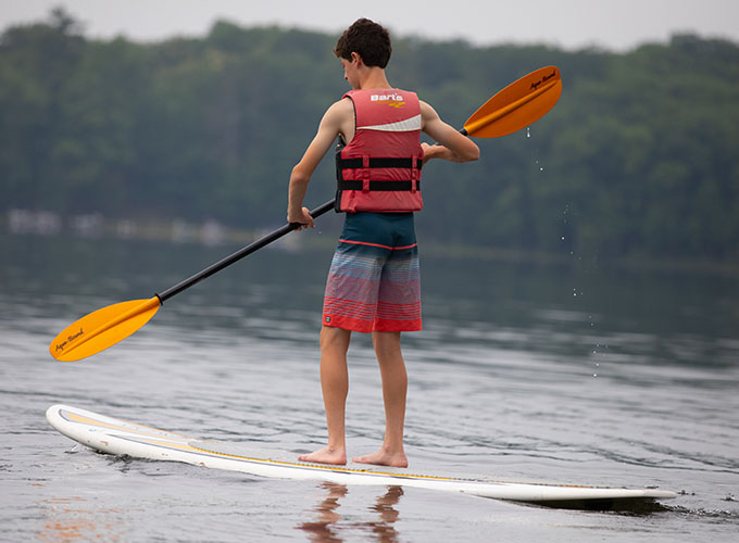 A camper wears a life jacket and stand-up paddleboards on Spider Lake at North Star Camp for Boys.