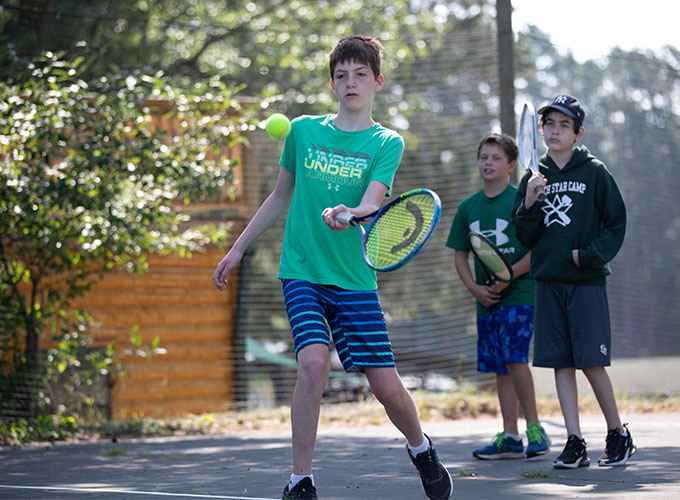 A camper prepares to swing a tennis racquet at an incoming ball during a tennis lesson at North Star Camp for Boys.