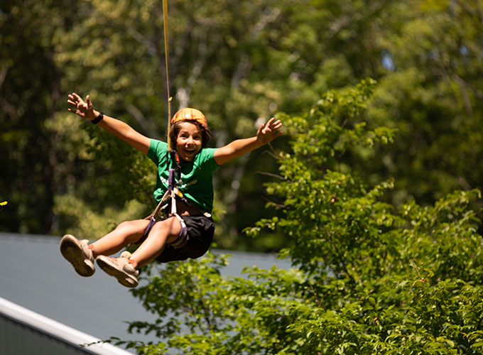 A camper excitedly glides through the trees while attached to the zipline at North Star Camp for Boys.