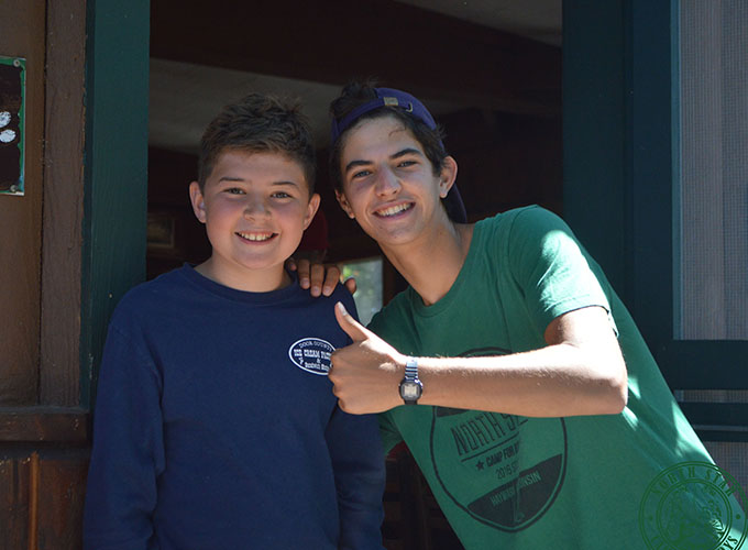 A camper and staff member at North Star Camp for Boys smile, the staff member is holding a "thumbs up".