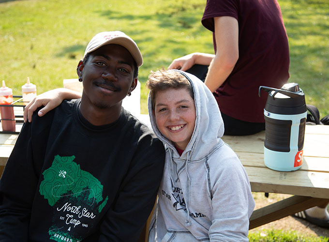 A camper and junior counselor smile while sitting together at a picnic table at North Star Camp for Boys.